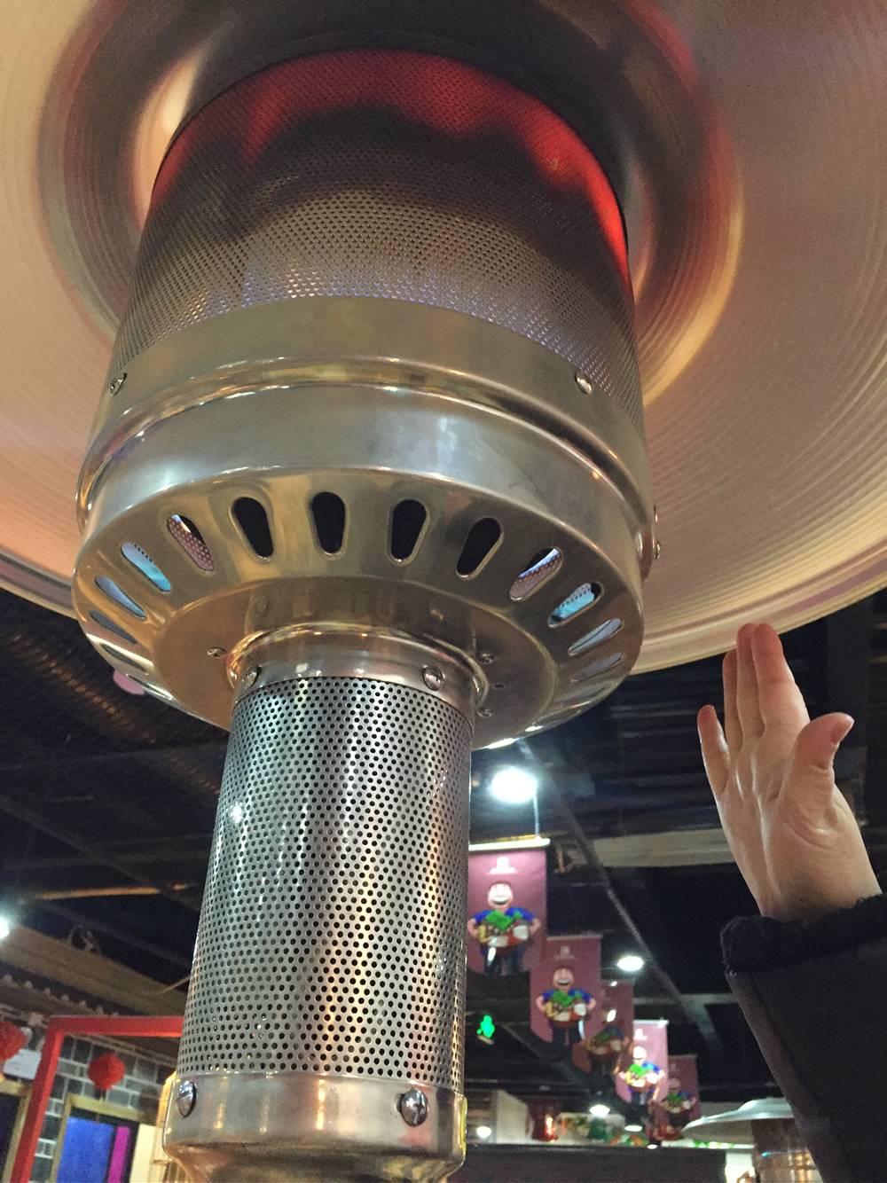 A hand is warmed by a round hole perforated stove with flames in a theme restaurant.