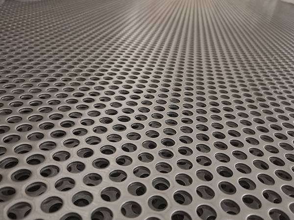 A piece of stainless steel round hole perforated sheet with a metal coin on its surface.