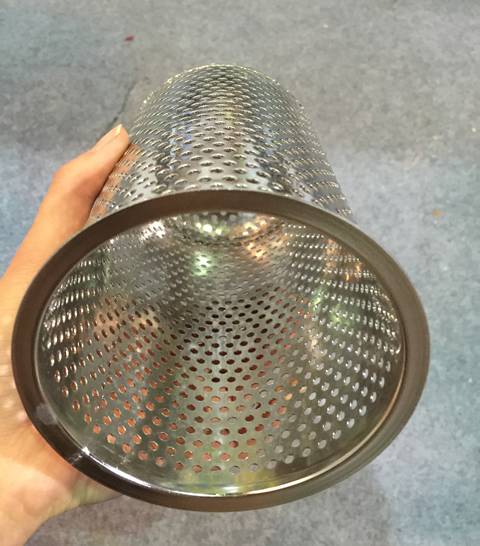 Une main tient un filtre à cylindre avec des trous ronds perforés et un bord enveloppé en acier inoxydable.