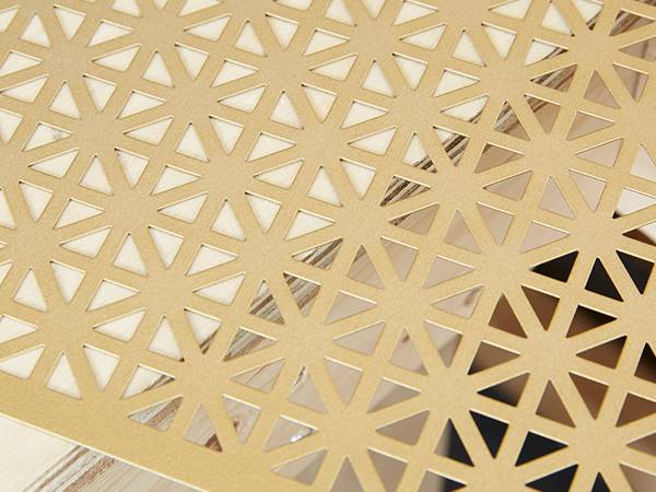 Una hoja de latón perforada con muchos agujeros triangulares perforados en una mesa