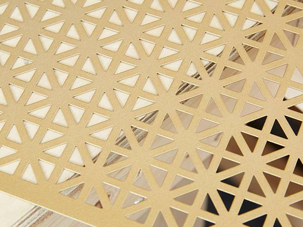 A perforated brass sheet with many triangular punched holes on a table