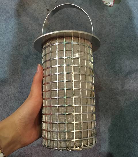 Une main tient un filtre à panier avec des trous carrés perforés à l'extérieur et un treillis métallique tissé à l'intérieur.